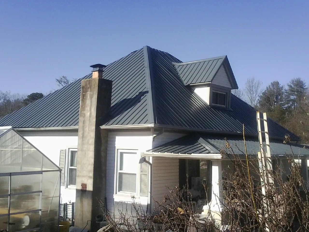 Dark blue standing seam metal roof on a white farmhouse with dormer — Slate & Tile Roof Repair by Roofing Brothers in Adkins