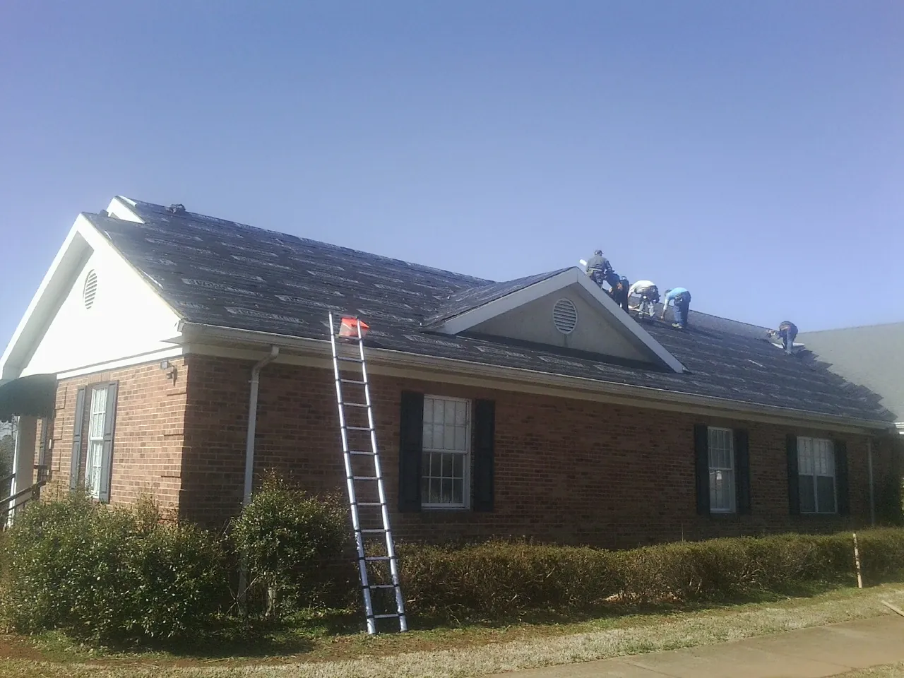 Crew tearing shingles off a brick ranch roof with a ladder set — Emergency Roof Repair work by our crew in Adkins