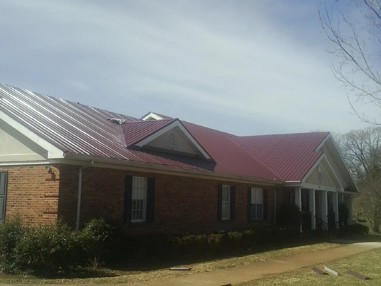 Red metal roof with gabled entries on a long brick building, from a Hail Damage Roof Repair job in Adkins