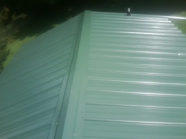New green metal panels meeting at the ridge of a roof — Flat Roof Repair work by our crew in Adkins