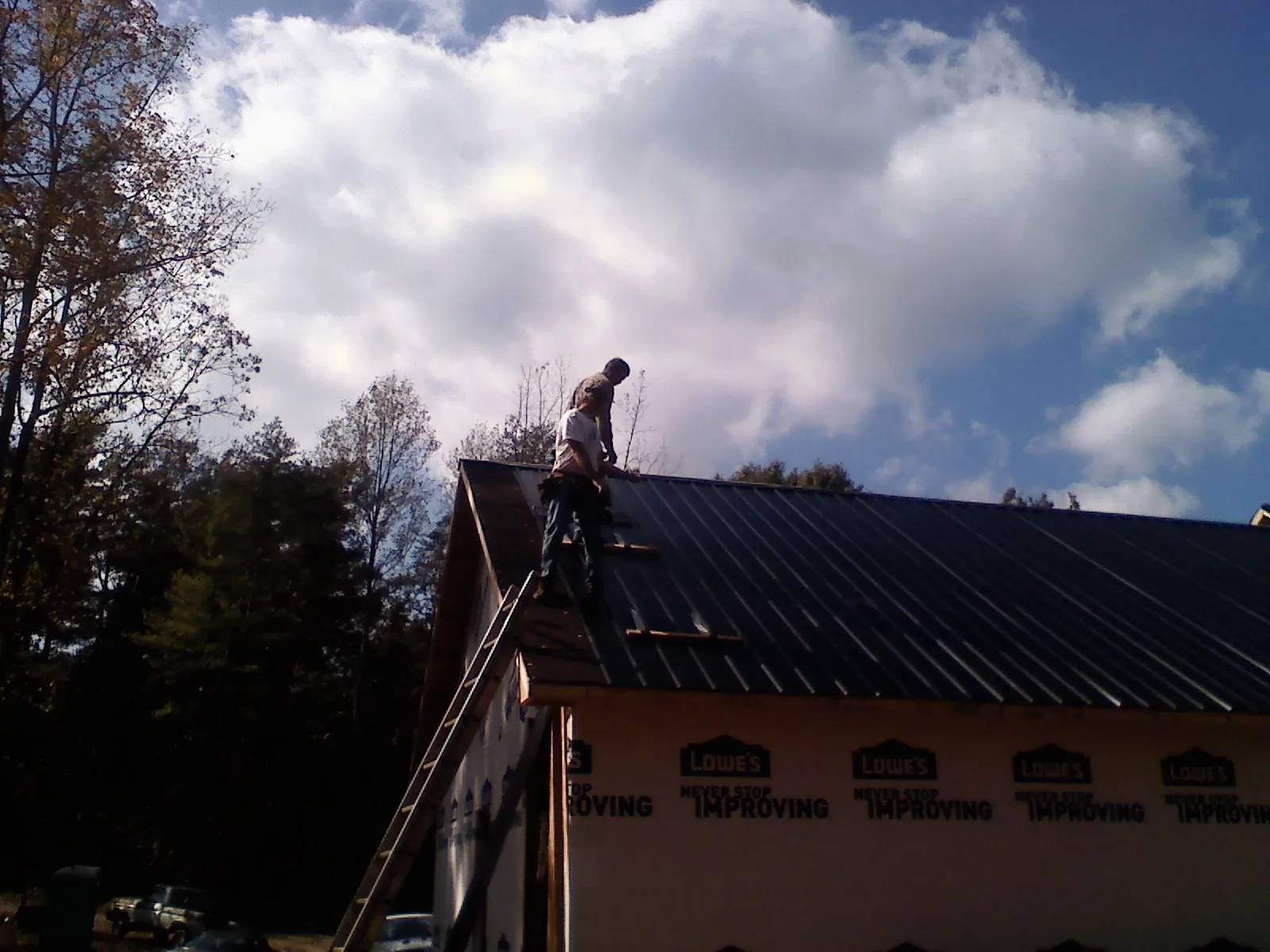 Roofer fastening dark metal panels high against a cloudy sky, from a Roof Inspection job in Adkins