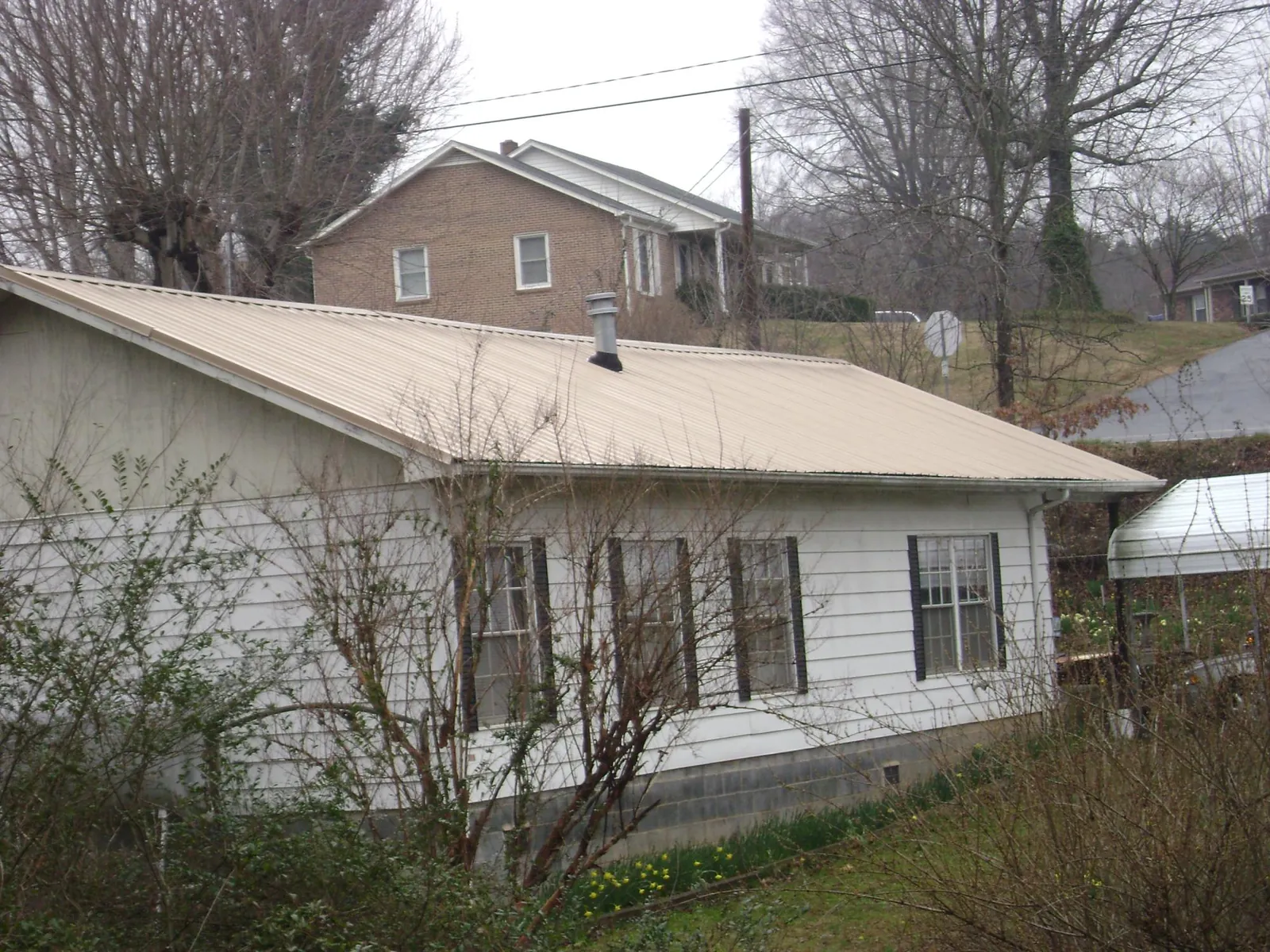 Tan metal roof on a white sided house set into a hillside — Commercial Roofing by Roofing Brothers in Adkins